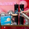 A festive setup with "Galentine's" neon sign, balloons, disco balls, and a cart holding cream chargers, a whipped cream dispenser, and a cocktail.