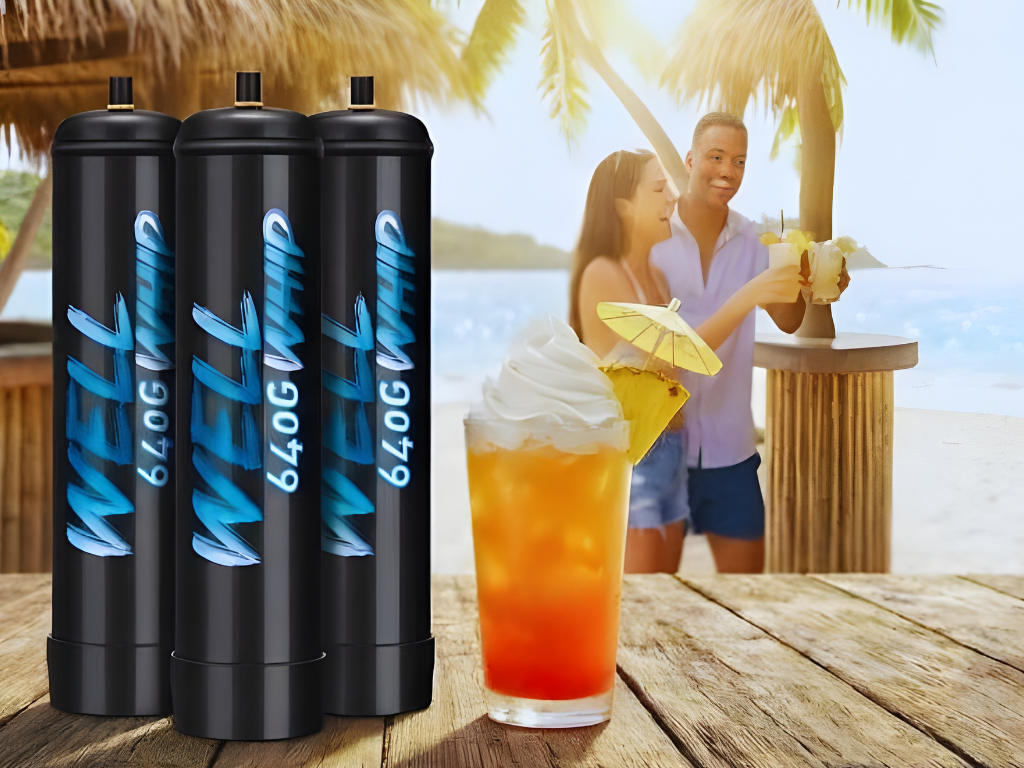 Three black canisters labeled "WELL 640G WHIP" stand on a wooden table with a tropical drink in the foreground. A smiling couple enjoys drinks by the beach.