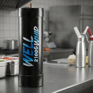 Tall black canister labeled "WELL 2100GWhip" stands on a stainless steel kitchen counter. Whipped cream canisters and food trays are in the background.