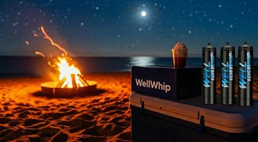A beach bonfire at night under a starry sky, near a cooler with whipped cream canisters and a paper cup. The scene conveys warmth and relaxation.